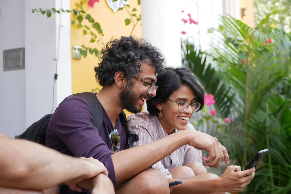 Two friends laughing together while looking at a phone outdoors